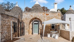 A stone building with a central archway, a white tent, and a small outdoor seating area. - Trulli Trullò in Locorotondo, Locorotondo, Italy (Locorotondo)