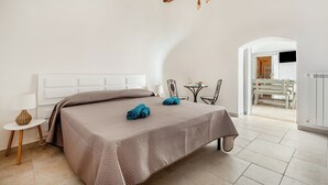 A bedroom with a bed, a small table, a chair, and a view of a dining area. - Trulli Trullò in Locorotondo, Locorotondo, Italy (Locorotondo)