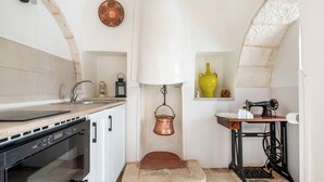 A compact kitchen with a built-in oven, a sink, a hanging copper pot, and a vintage sewing machine. - Trulli Trullò in Locorotondo, Locorotondo, Italy (Locorotondo)