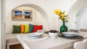 A dining area with a table set for two, a green vase with yellow flowers, and a sofa with colorful cushions. - Trulli Trullò in Locorotondo, Locorotondo, Italy (Locorotondo)