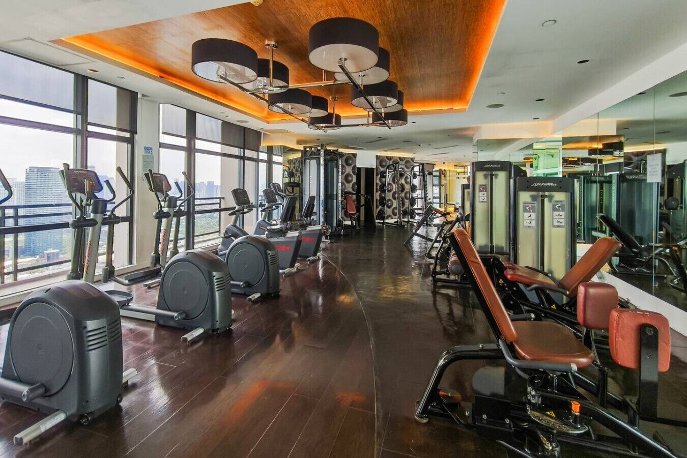 Een sportschool met cardioapparatuur, gewichthefapparatuur en grote ramen met uitzicht over de stad.