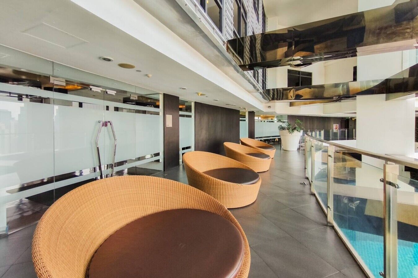 Een moderne lobby met glazen balustrades, rieten zitplaatsen en een zwembad.