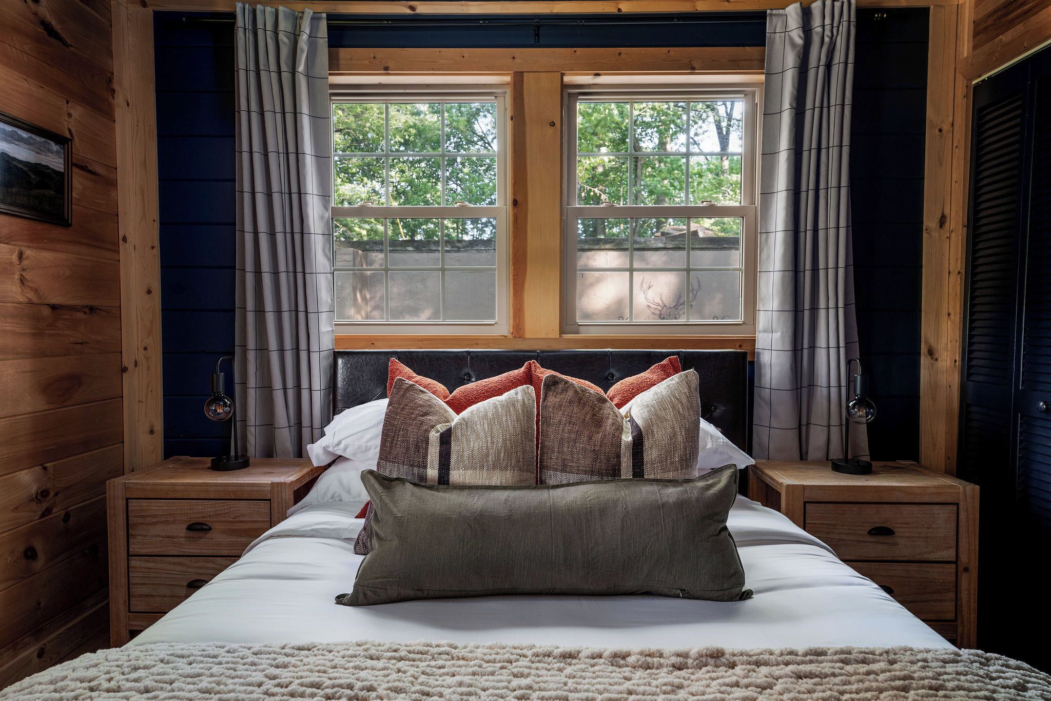 A wooden cabin-style bedroom with a bed, two nightstands, and a window with curtains.
