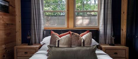 A wooden cabin-style bedroom with a bed, two nightstands, and a window with curtains.