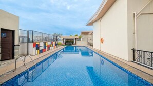 En swimmingpool med flisebelagt område, et metalhegn og en dør med et skilt.