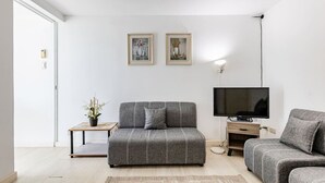 A modern living room with a sofa, a TV, a small table with a plant, and two framed pictures on the wall. - StayHere 2BR Beach Tropical City Getaway Azure (Parañaque)
