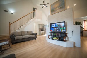 A living room with a sofa, a TV mounted on a brick wall, a staircase, and a kitchen in the background. - A Quiet Lakefront Retreat for Relaxed Getaways (Oak Point)
