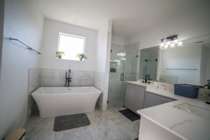 A modern bathroom with a freestanding bathtub, a glass-enclosed shower, a vanity with a mirror, and a window with plants. - A Quiet Lakefront Retreat for Relaxed Getaways (Oak Point)