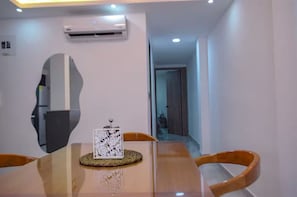 A dining area with a glass table, wooden chairs, a decorative centerpiece, an air conditioning unit, and a hallway leading to another room. - Modern and quiet : 2Bdrm. clinic and stadium area (Cali)