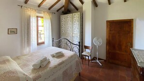 Quarto com cama, cadeira, ventilador, guarda-roupa e porta.