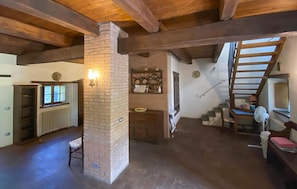 A rustic interior with exposed wooden beams, a brick fireplace, a staircase, and a shelf with kitchenware. - Gorgeous home in Villa Collemandina (Villa Collemandina)