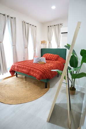 Ein Schlafzimmer mit einem Bett, einem runden gewebten Teppich, einem grünen Kopfteil und einem Blumentopf.