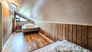 A bedroom with a wooden floor, a bed, a window, and a ceiling with a light fixture.