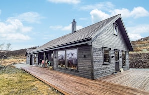 A modern wooden house with large windows, a deck, and a chimney.