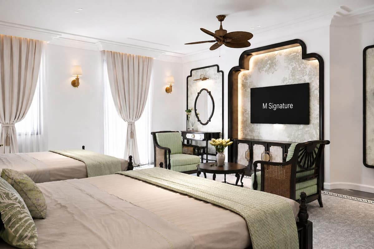 A hotel room with two beds, a ceiling fan, a wall-mounted TV, and a seating area with chairs and a table.