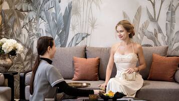 A room with a sofa, cushions, a vase with flowers, and a tray with a glass and a lime.