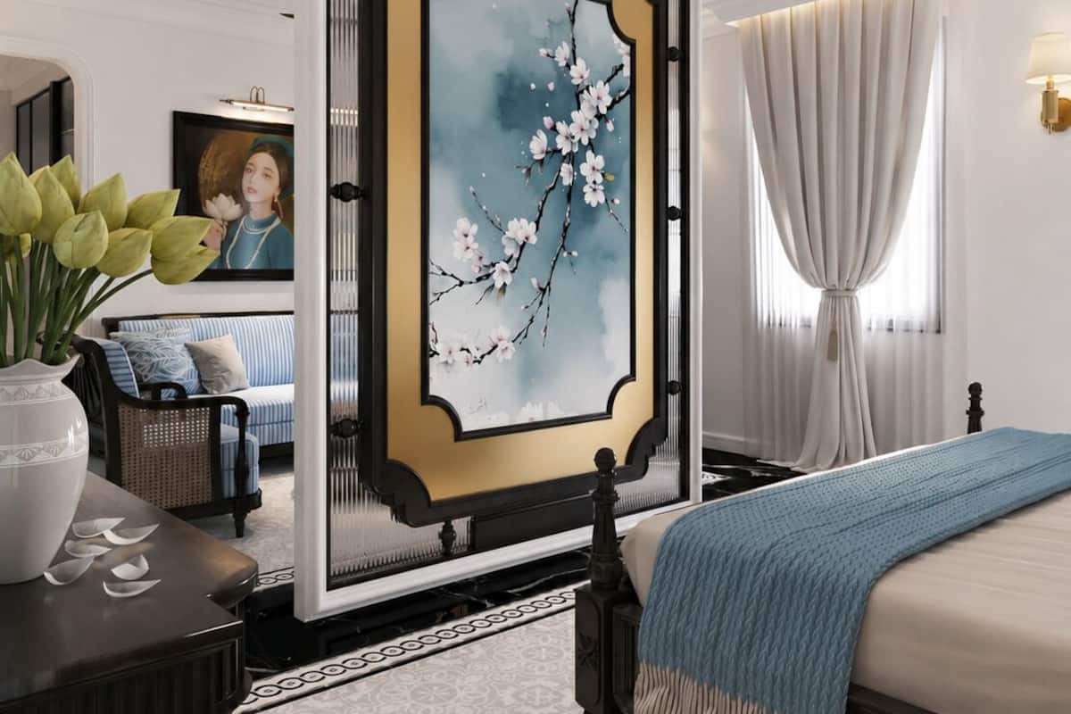 A modern bedroom with a large painting, a bed with a blue blanket, a desk with a vase, and a chair.