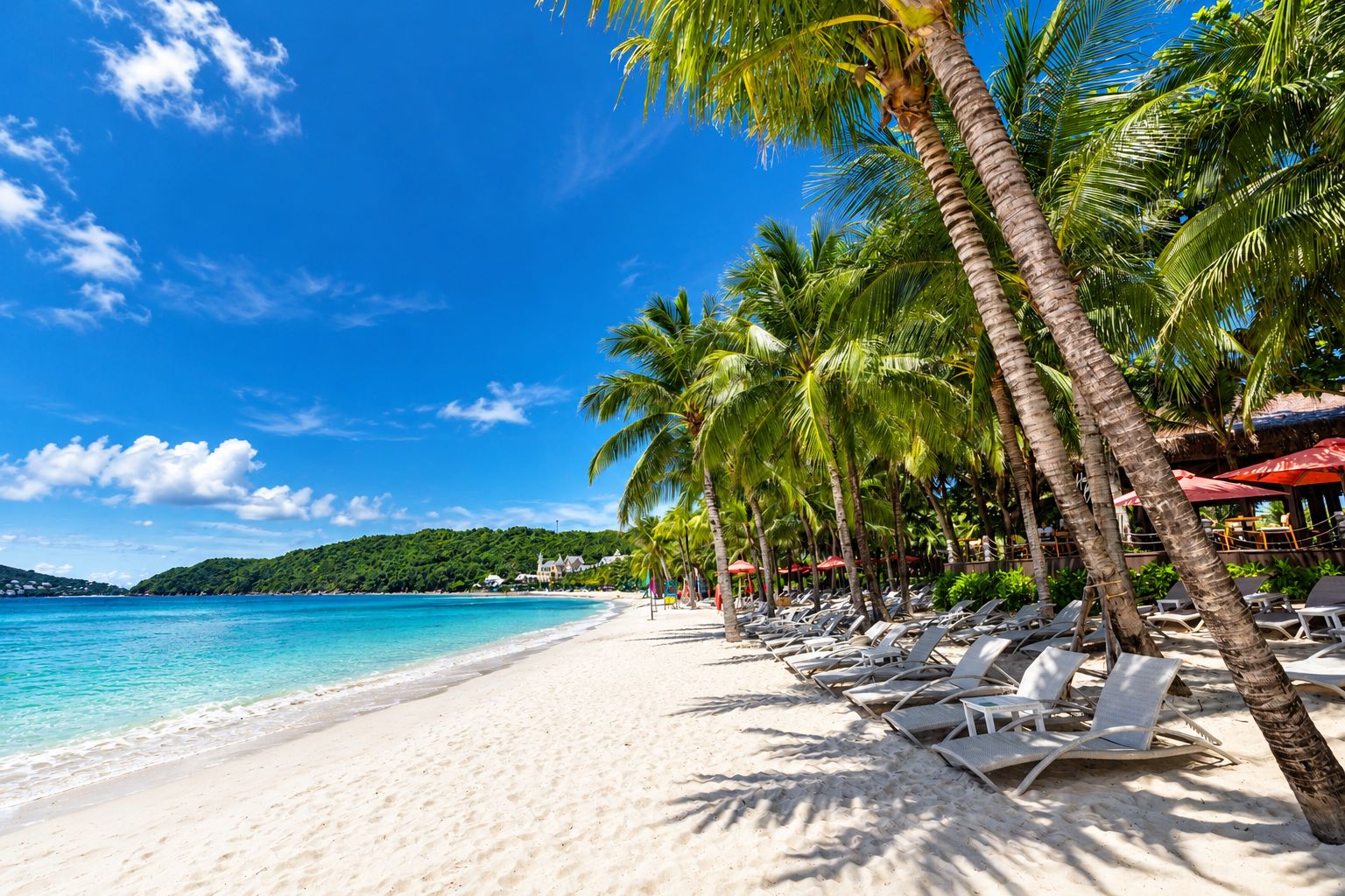 Una playa con arena blanca, palmeras y agua cristalina azul.