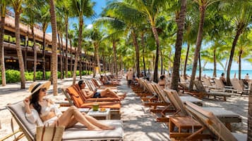Un resort frente a la playa con filas de tumbonas y palmeras, un edificio con balcones y una vista despejada del mar.