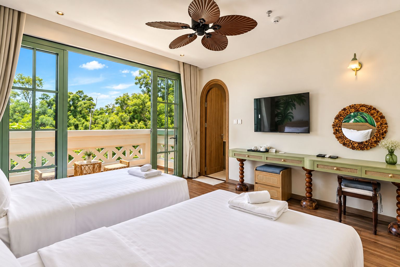 Une chambre d’hôtel avec deux lits, un bureau, une télévision et un balcon donnant sur un paysage arboré.