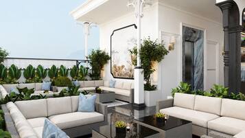 A modern outdoor seating area with sofas and a coffee table, surrounded by potted plants and a wall-mounted artwork.