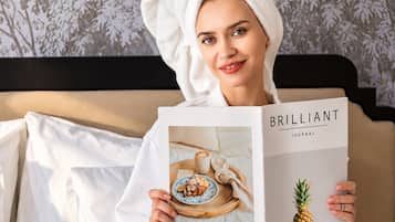 A person sitting on a bed with a book titled 'BRILLIANT JOURNAL' and a tray with pastries.