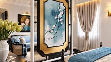 Een hotelkamer met een groot bed, een bijzettafeltje met een bloevas, een schilderij van een tak en een uitzicht op een stadsbeeld door het raam.