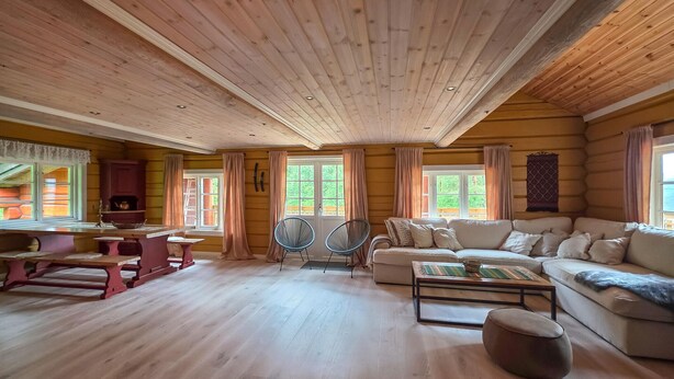 Interior de una cabaña de troncos con techo de madera, un sofá, una mesa y una silla.