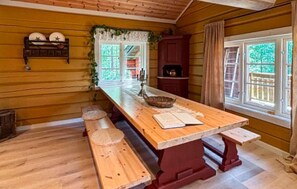 A wooden interior with a long dining table, benches, a window with curtains, and a shelf with decorative items. - Lovely home in Prestestranda with sauna (Prestestranda)