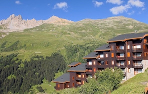 Un edificio de varios pisos con balcones, frente a un paisaje montañoso.
