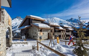 Ein Chalet mit Steinmauern und Holzdächern, umgeben von schneebedeckten Bergen.