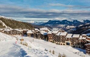 Un centro de esquí con edificios de estilo chalet, laderas nevadas y montañas al fondo.