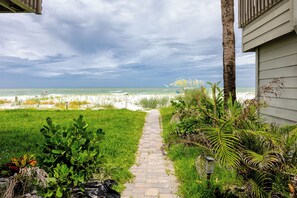 Ein Pfad führt zu einem Strand mit Blick auf das Meer und einem Gebäude mit Schrägdach.