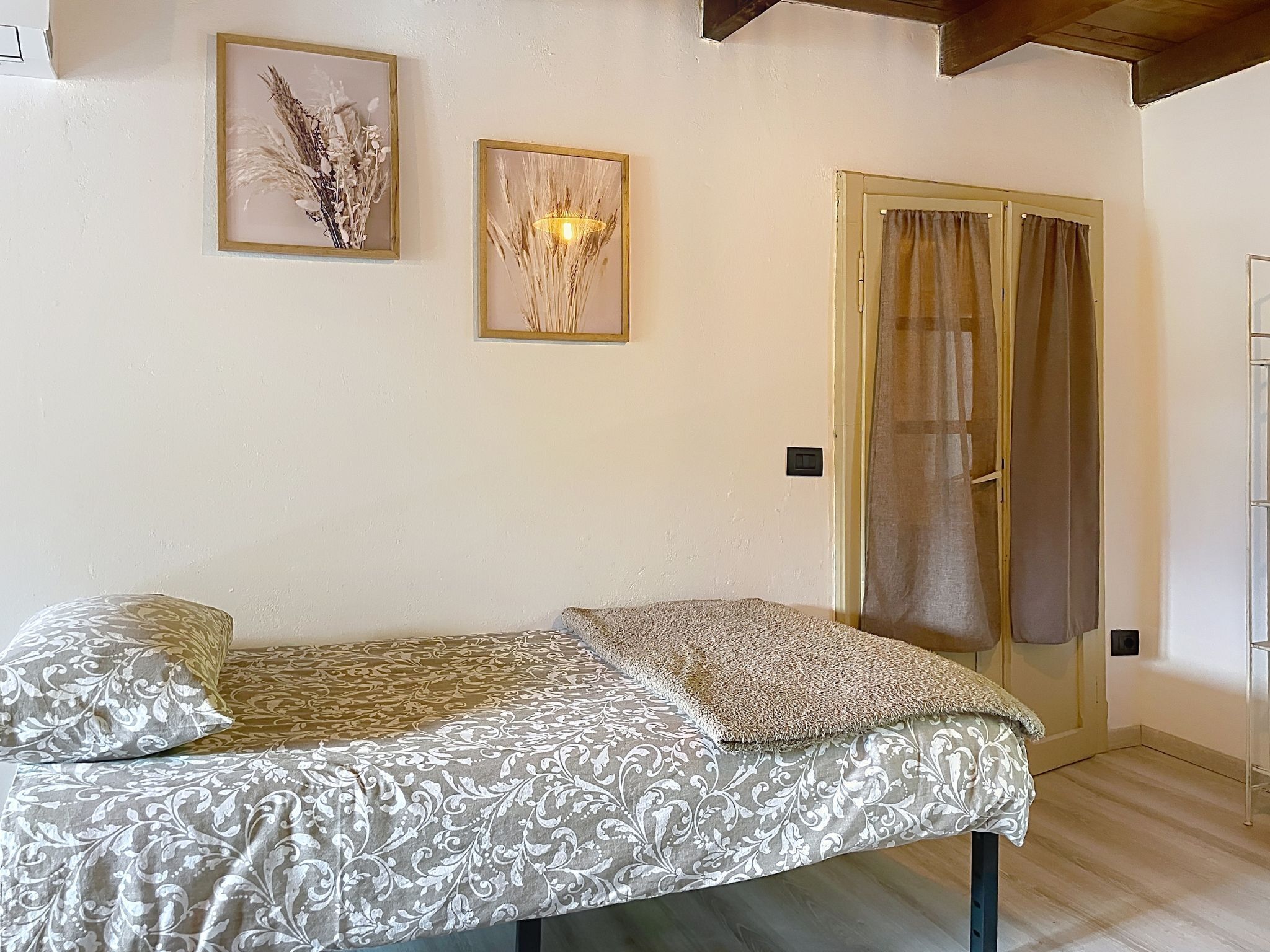 A room with a bed, two framed pictures on the wall, a door with curtains, and a light switch.
