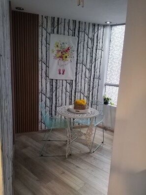 Ein Essbereich mit einem runden Tisch, zwei Stühlen, einer Wand mit Baumstruktur und einem Fenster mit Pflanze.