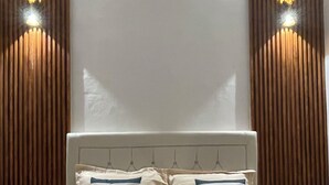 A bed with a headboard, two pillows, and a wall with vertical wooden slats and two wall-mounted lights. - Saren Muding, a private, charming 2BR corner house in Kerobokan. (Tabanan, Tabanan Regency)
