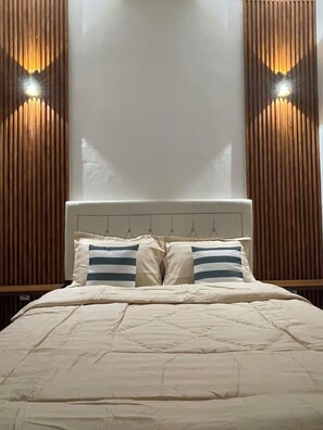 Ein Bett mit Kopfteil, zwei Kissen sowie eine Wand mit vertikalen Holzlatten und zwei Wandleuchten.
