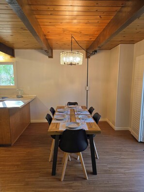 Ein Essbereich mit einem Holztisch, gedeckt für sechs Personen, schwarzen Stühlen, einer Kandelaber und einer Küchenzeile mit einem Fenster.