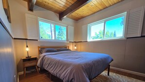 Ein Schlafzimmer mit einem Bett, zwei Nachttischlampen, einem Nachttisch, einem Fenster mit Jalousien und einem gemusterten Teppich.