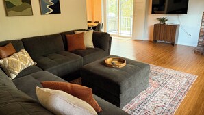 Ein modernes Wohnzimmer mit einem Ecksofa, einem Holztisch und einem großen Flachbildfernseher an der Wand.