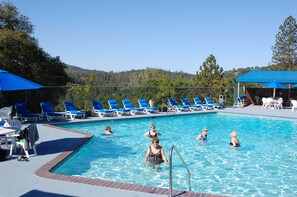 A swimming pool with blue chairs and umbrellas, surrounded by trees and hills.