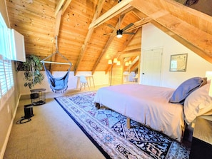 Ein gemütliches Schlafzimmer im Dachgeschoss mit Bett, Hängesessel und großem Teppich.