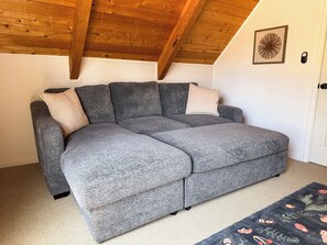A grey sectional sofa with two cushions, a wooden ceiling, a white door, and a patterned rug.