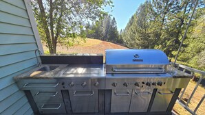 Eine Outdoor-Küche aus Edelstahl mit integriertem Spülbecken, Grill und mehreren Kochfeldern.