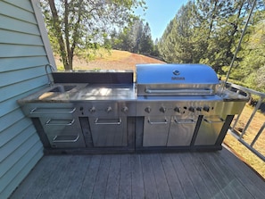Et udendørs køkken i rustfrit stål med vask, grill og flere gasblus.