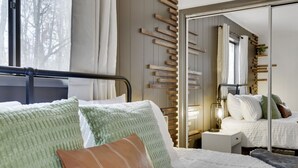 A neatly made bed with pillows, a bedside table with a lamp, and a mirror on the wall. - Mtn Retreat |Hot tub |Firepit |Theatre& Game Rooms (Tobyhanna)