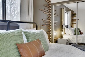 Ein ordentlich bezogenes Bett mit Kissen, ein Nachttisch mit Lampe und ein Spiegel an der Wand.