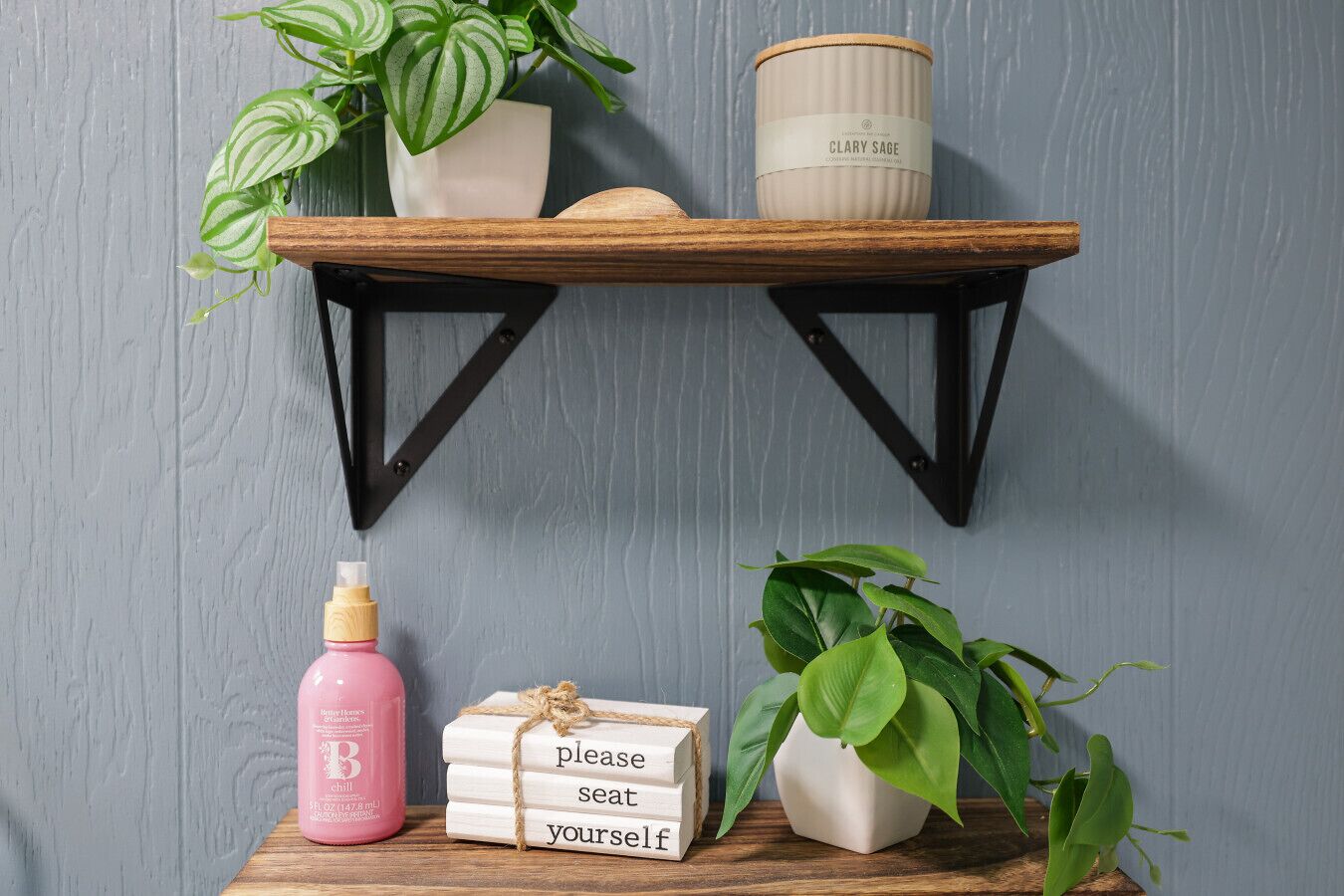 Una estantería con una planta, una vela, una botella y un cartel que dice 'Por favor, tome asiento'.