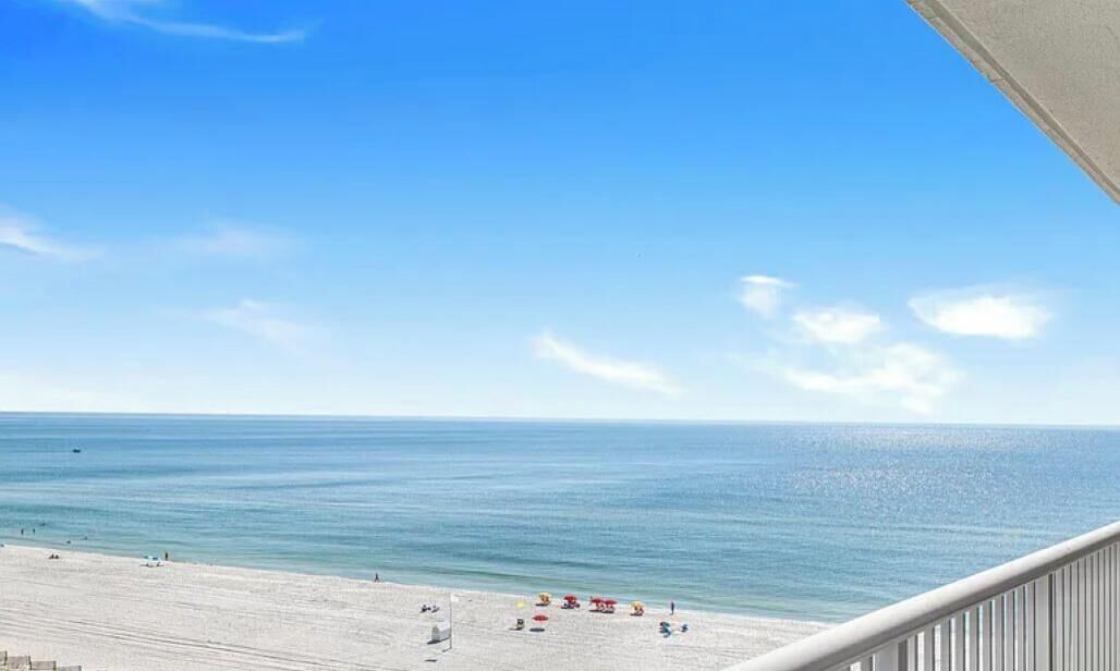 Vista sulla spiaggia con cielo sereno, mare calmo e una battigia sabbiosa con lettini e ombrelloni.