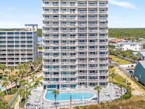 Ein mehrstöckiges Hotel mit Balkonen, einem Schwimmbad und umgebender Bepflanzung.